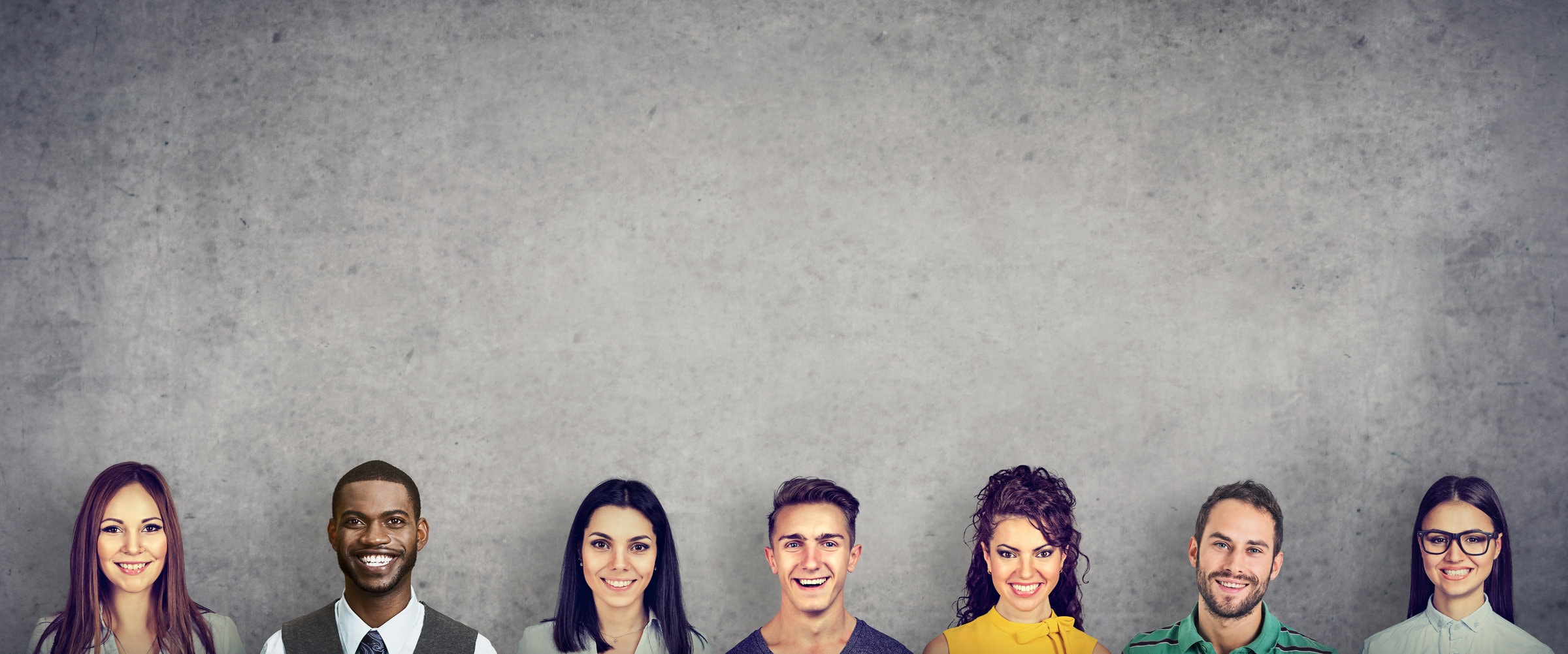 Group of content multiracial coworkers posing cheerfully at camera on gray wall