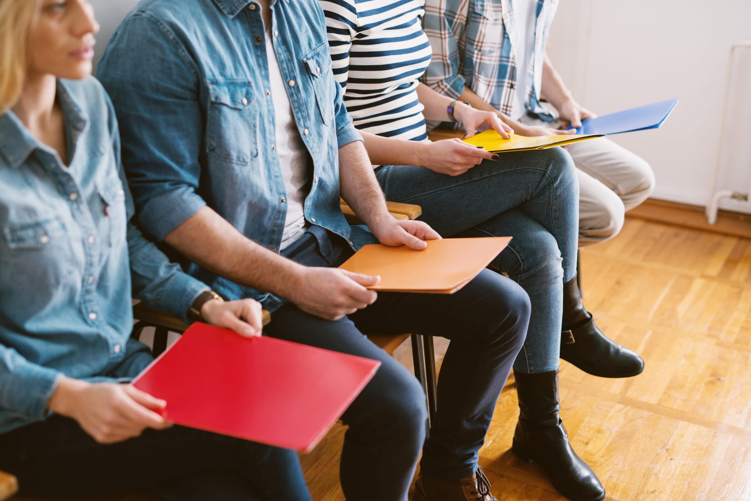 Close up view of young people sitting in chairs with folders bef Close up view of young people sitting in chairs with folders before the job interview in the waiting room.