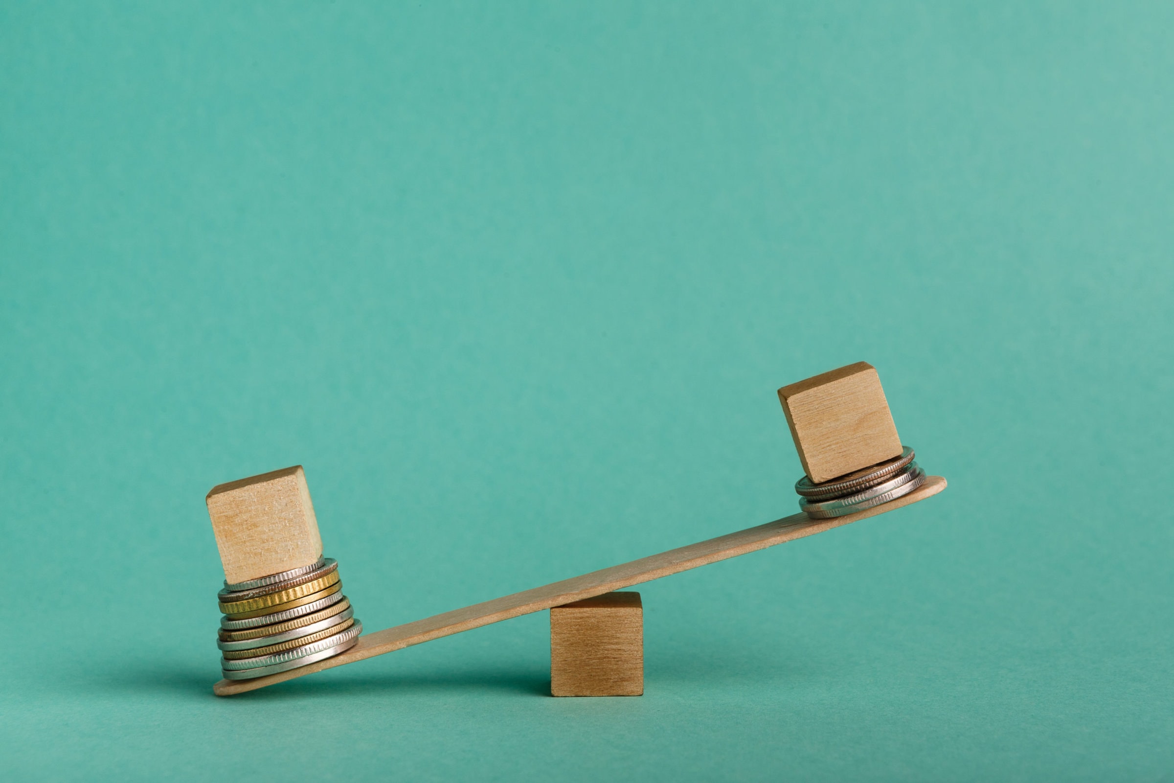 Pay gap and discrimination. Empty wooden cubes on seesaw with different stacks of coins, one outweigh, copy space