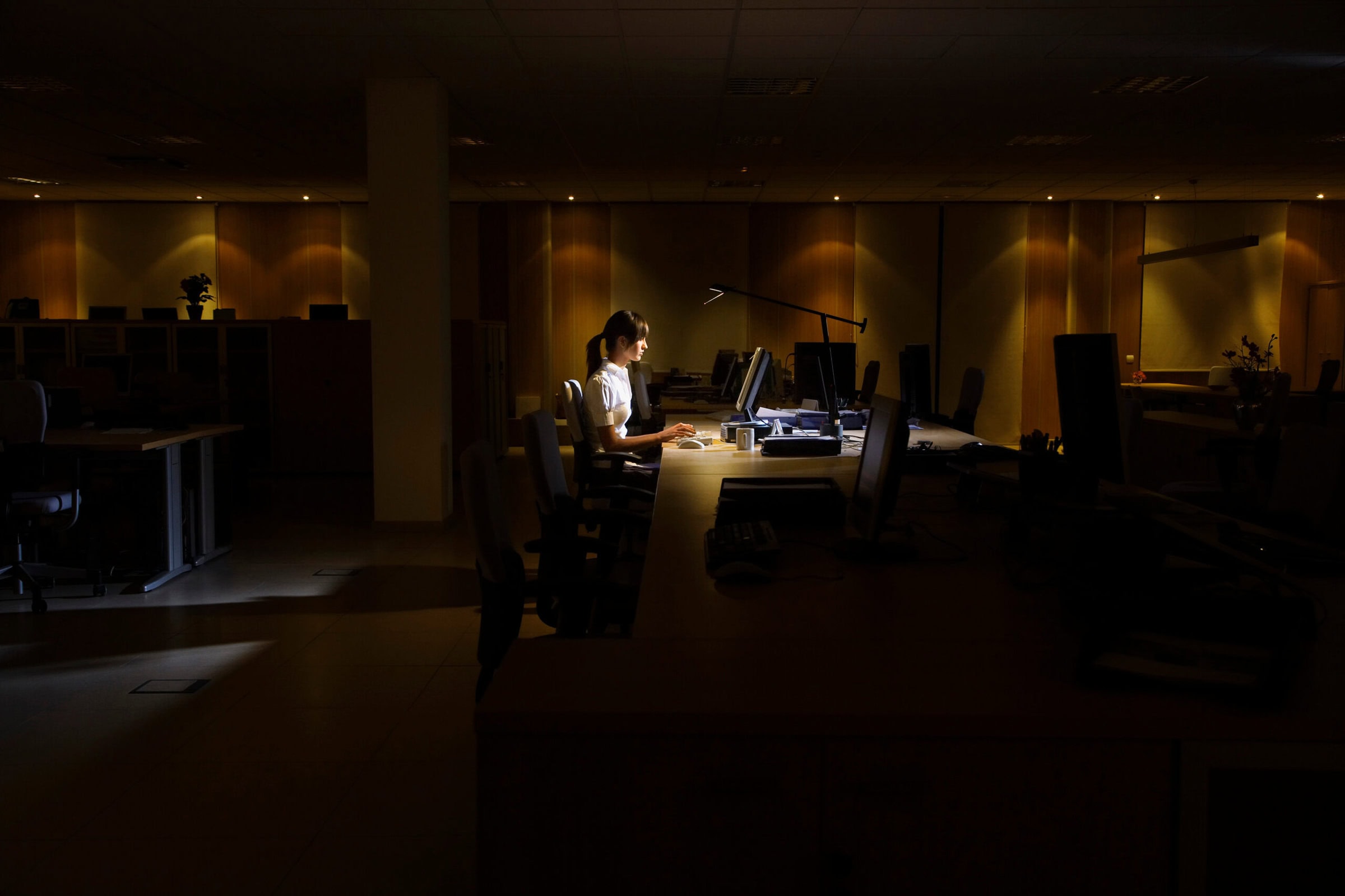 Side view of a young woman working on computer in dark office Side view of a young woman working on computer in dark office