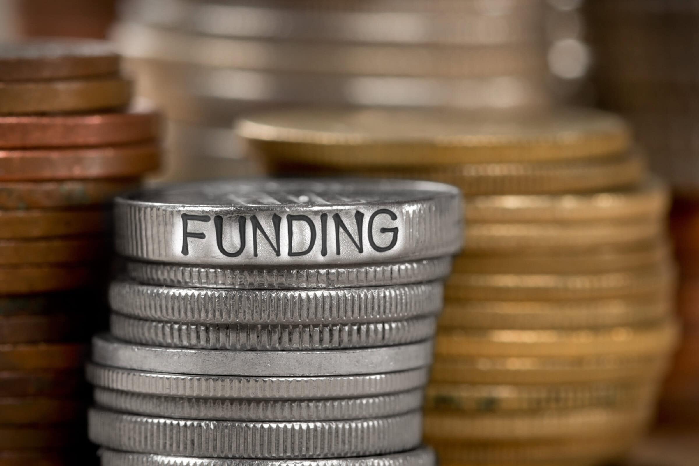 Photo of various stacks and rows of coins with FUNDING concept word imprinted on metal surface