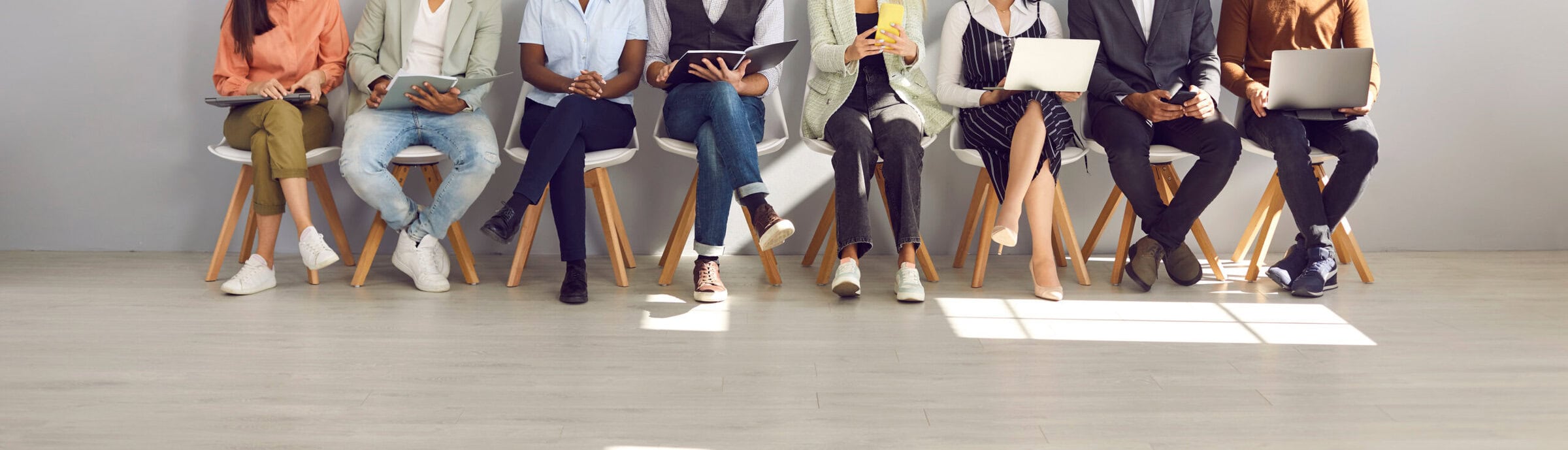 Diverse people waiting in line for their job interviews or business appointments Diverse people in smart casual clothes holding paper documents, CVs, resumes, laptops and cellphones waiting in line for job interviews or business appointments in recruitment agency, legs low section