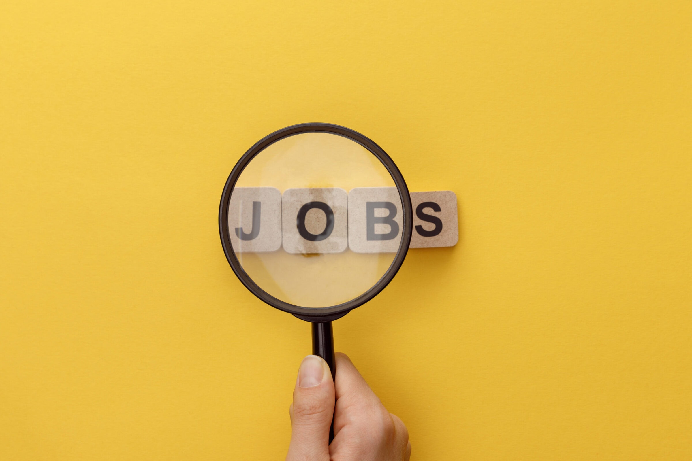 cropped view of woman holding magnifying glass under cardboard squares with jobs lettering on yellow background cropped view of woman holding magnifying glass under cardboard squares with jobs lettering on yellow background