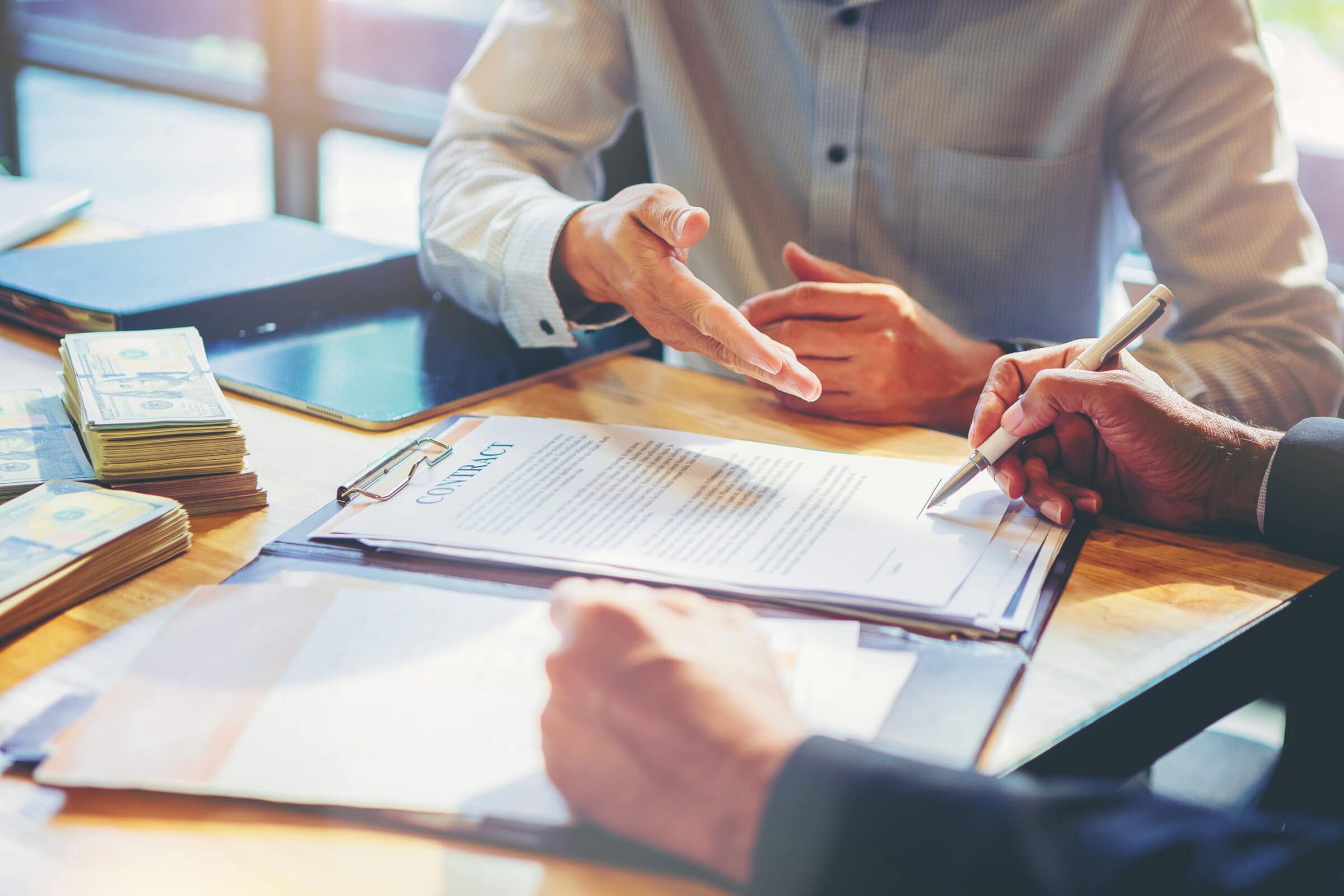 Businessman puts signature on contract at business meeting and passing money after negotiations with business partners.