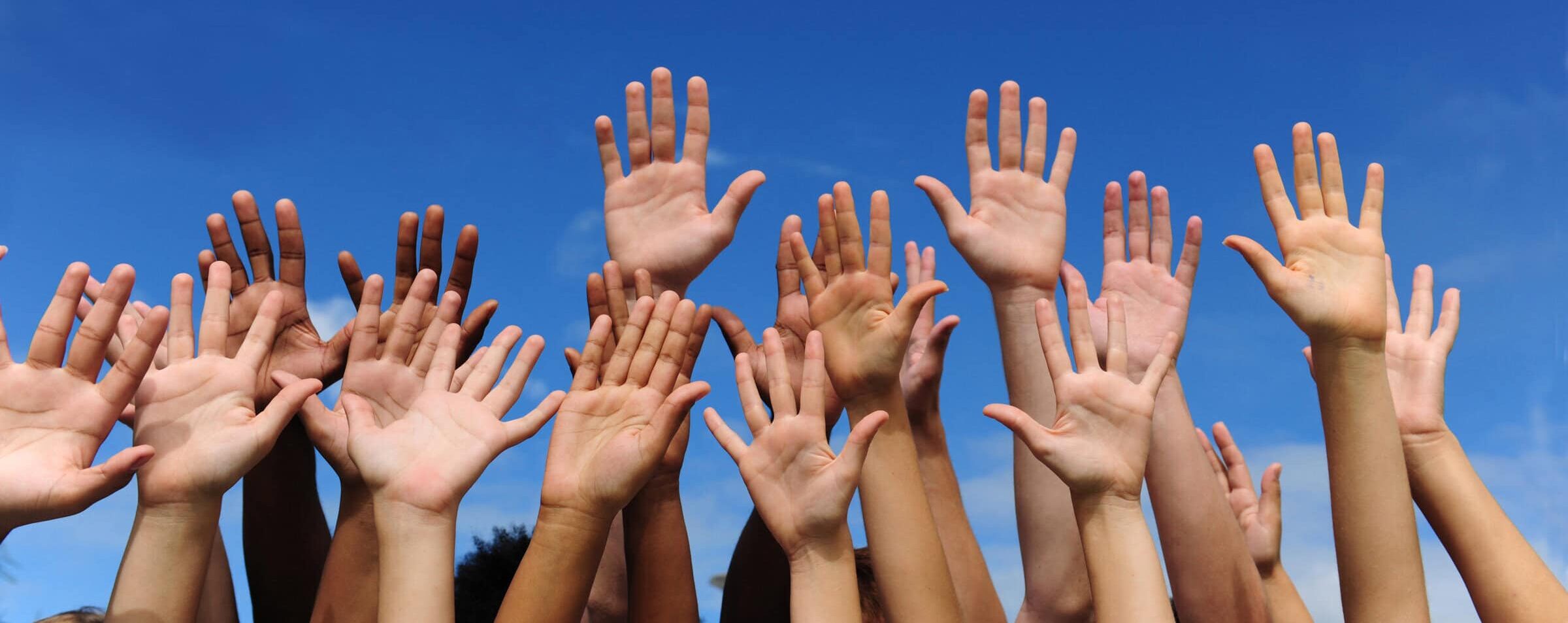 volunteer group raising hands against blue sky background