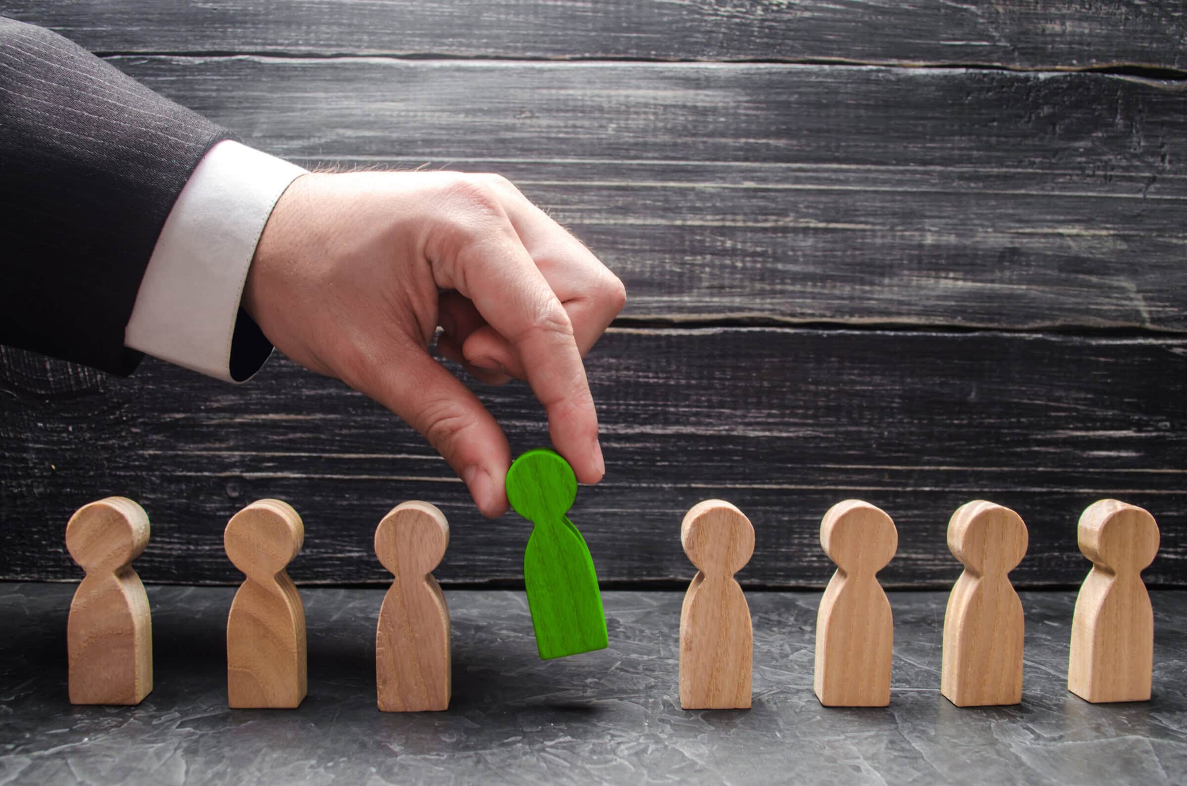 hand of a businessman takes a wooden figure of a man. The concept of search, hiring and firing workers, promotion. Business tactics and strategy, management, business management.