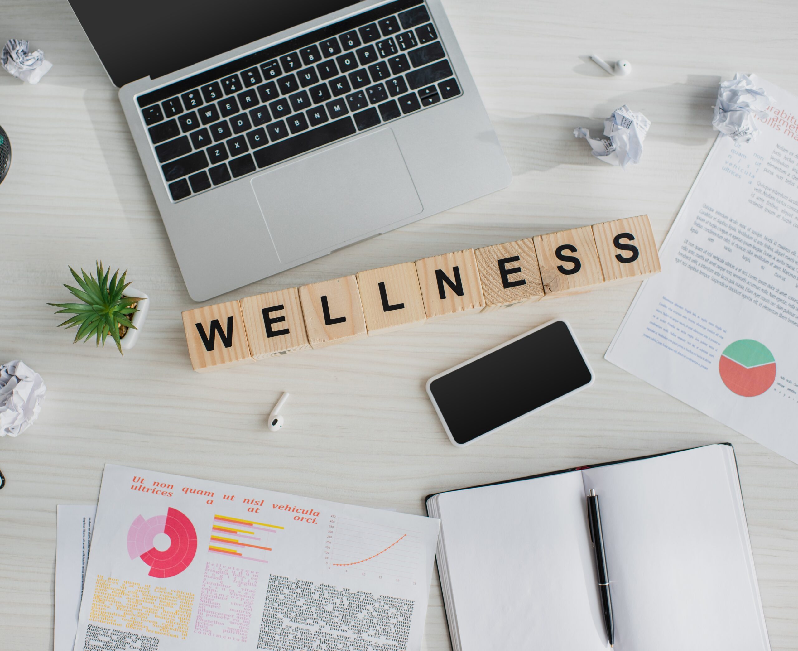 top view of workplace with business documents, laptop, smartphone and alphabet cubes with wellness word