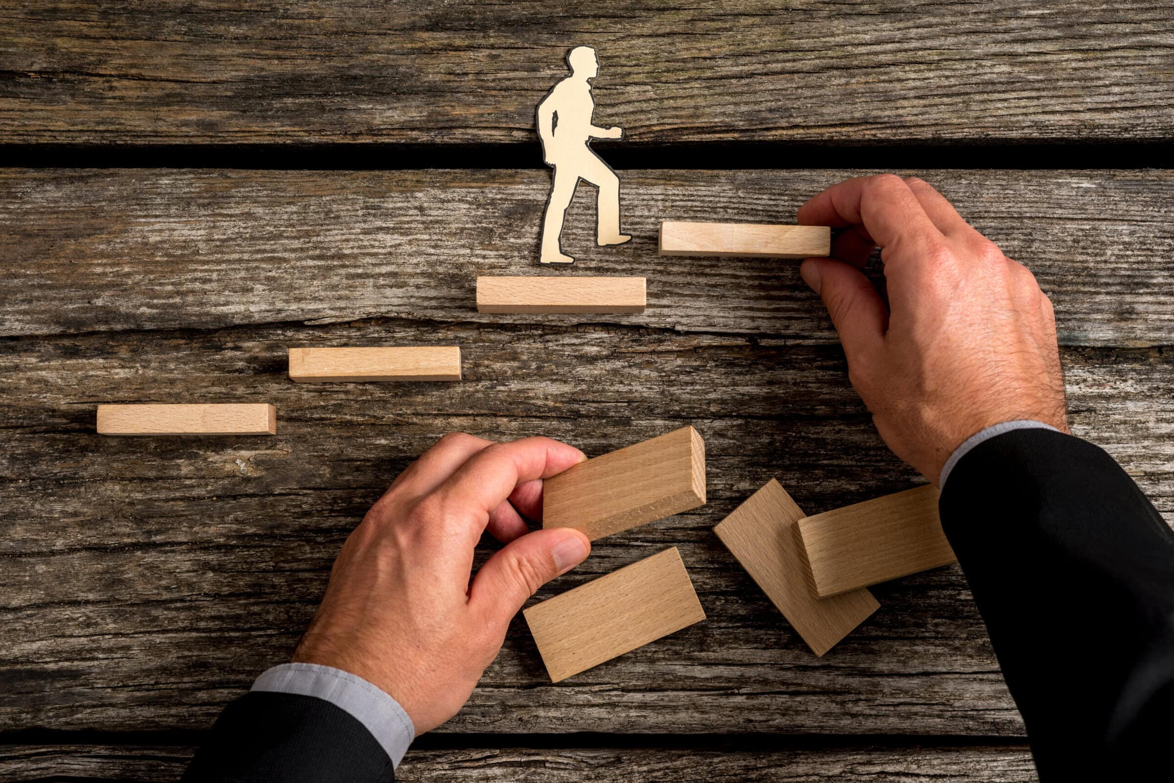 Conceptual image of personal and career promotion Silhouette cutouts of a man walking up steps, while the hand of other businessman building stairs for him in a conceptual image of personal and career promotion.